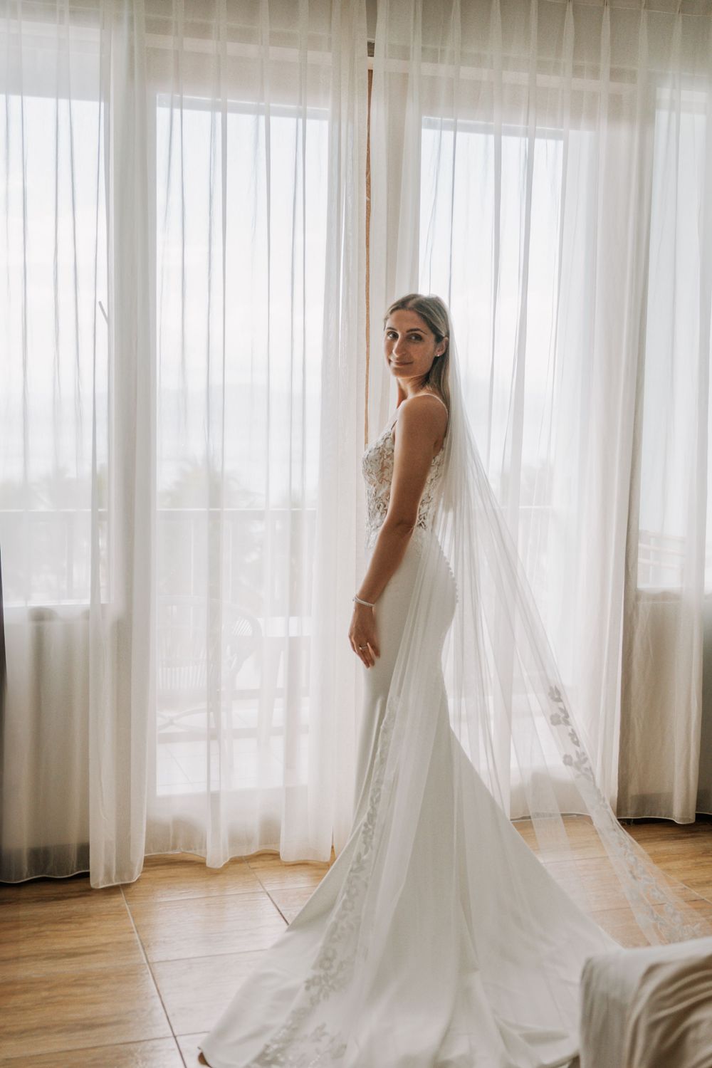 Bride in elegant white wedding dress and veil photographed in sequence against bright window with sheer curtains.