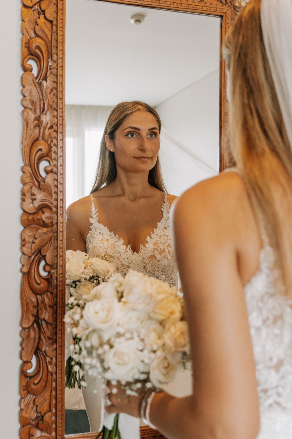 Ornate gold framed mirrors reflect a bride getting ready with white floral arrangements displayed.