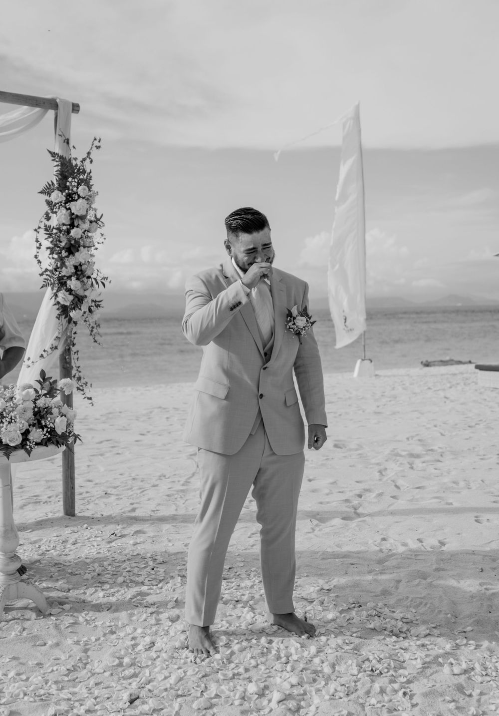 A heartwarming moment captured in black and white as a couple shares their first dance on a beach at their wedding ceremony.