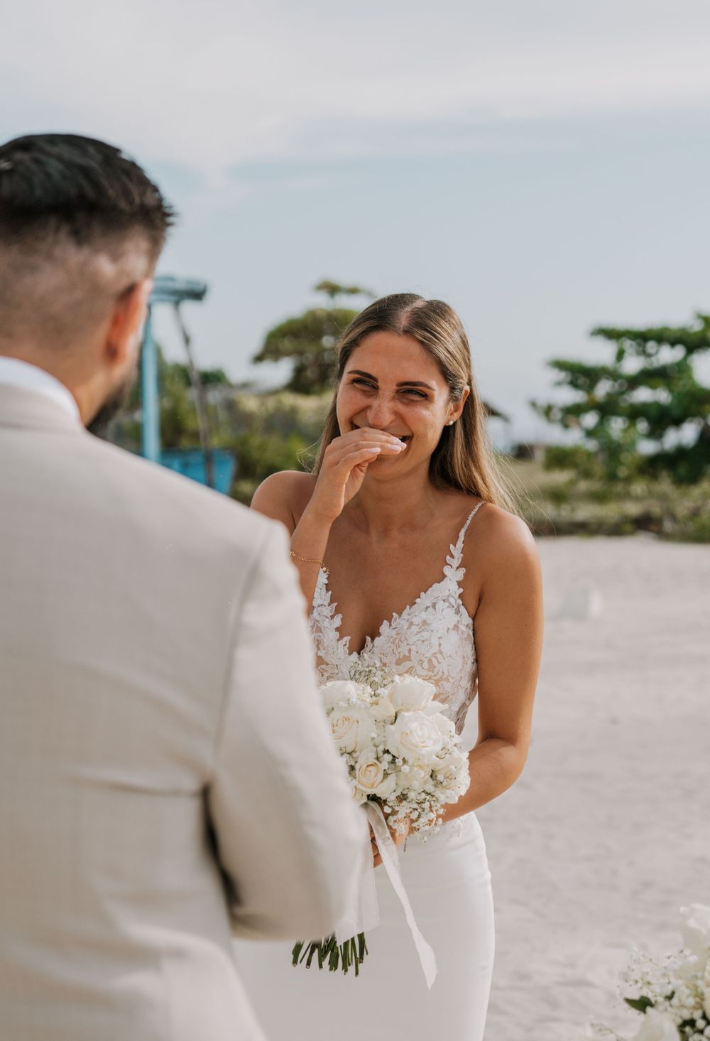 A beach wedding couple shares a candid moment during their seaside ceremony with white decor and flowers.