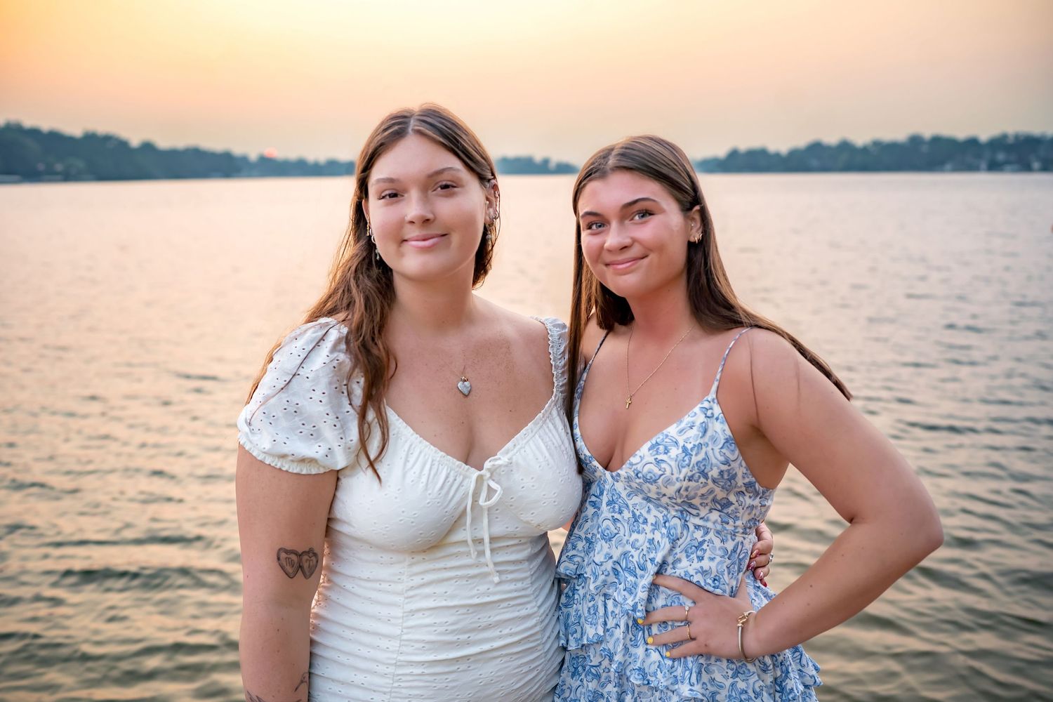 Two people pose together at golden hour by a serene lake in summer outfits.