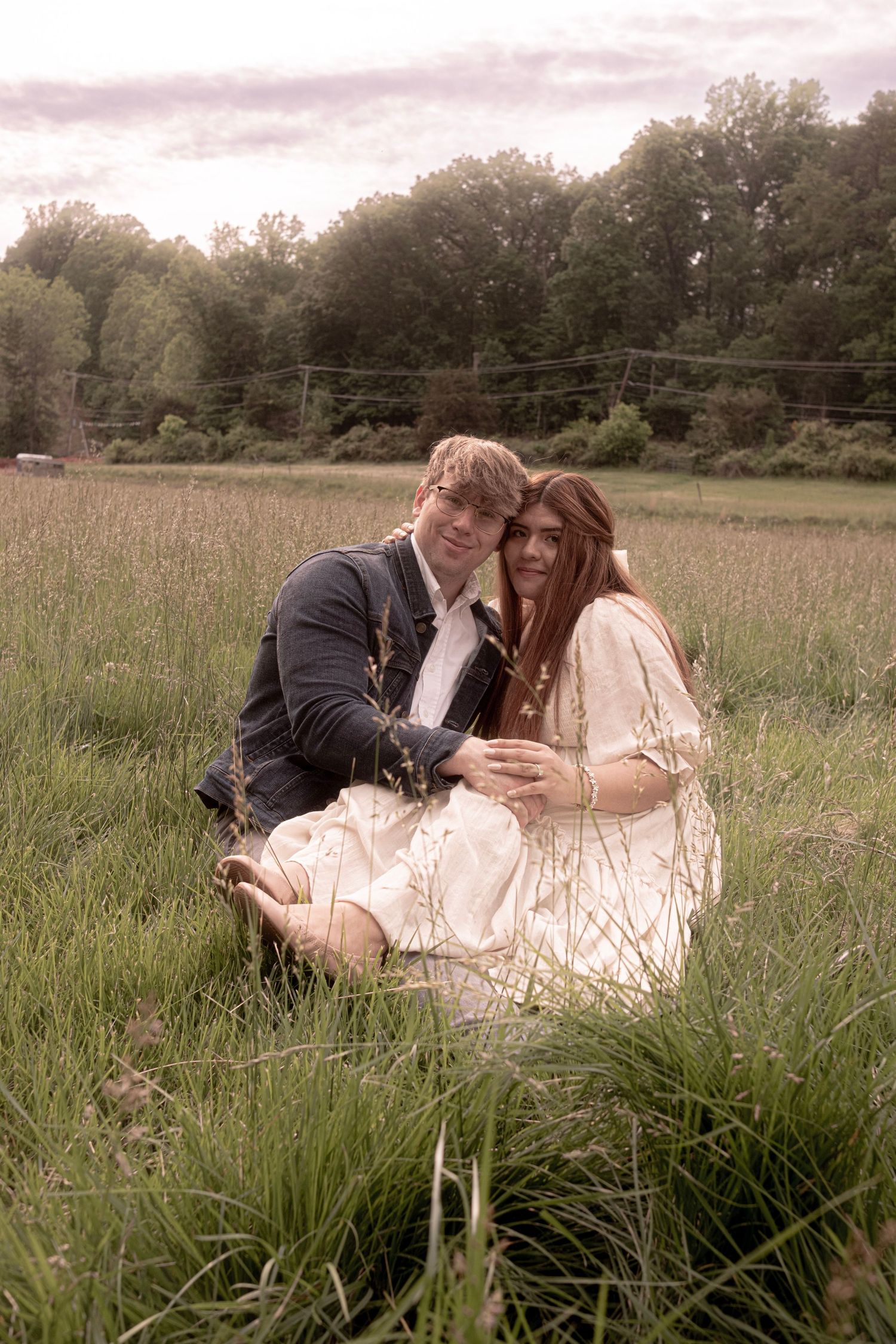 A couple enjoying a romantic moment while lying in a grassy meadow at sunset.