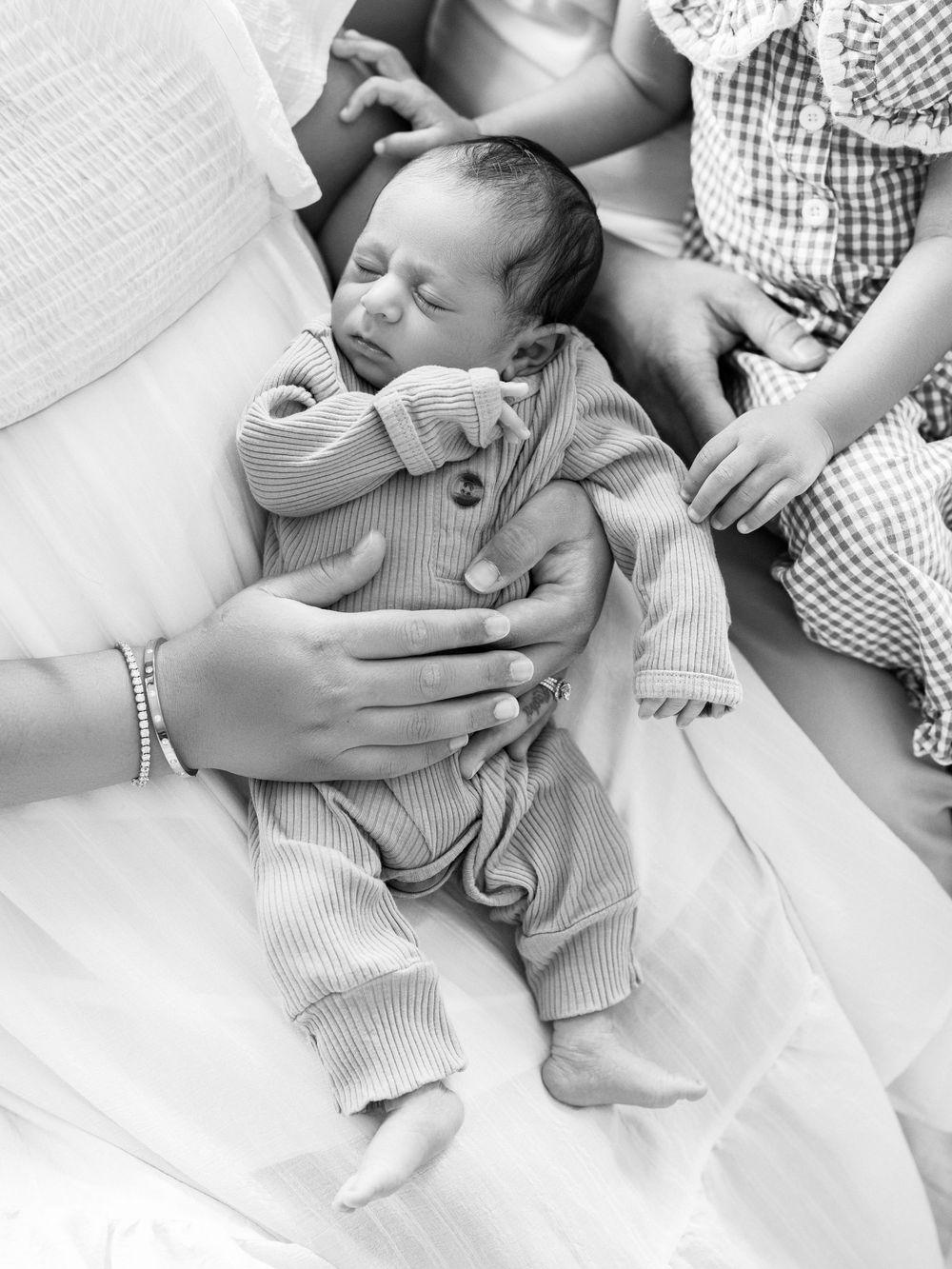Black and white photo of a newborn baby in a striped onesie cradled by loving hands on a white blanket.