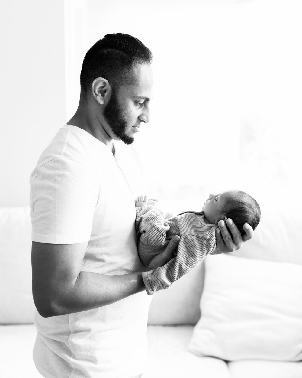 Black and white photo of a father tenderly cradling his newborn baby in his arms.
