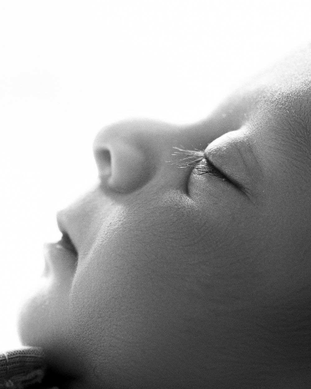 Close-up black and white profile portrait of a sleeping newborn baby with delicate eyelashes and soft skin.