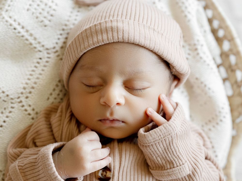 Peaceful newborn baby sleeping in a cozy knit outfit and beanie hat, with tiny hands near face.