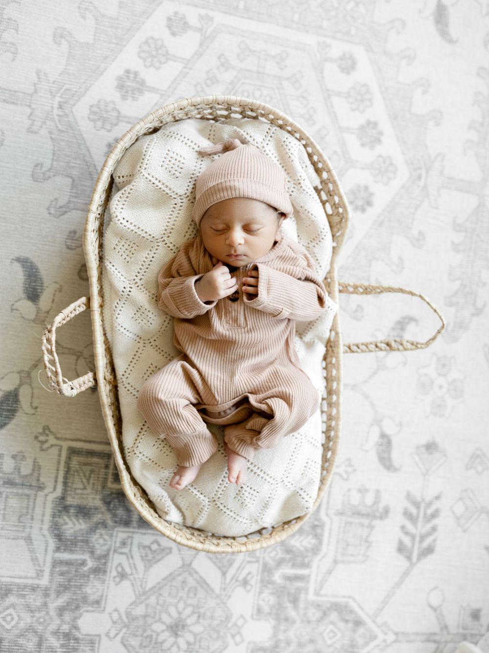 Sleeping newborn baby in a moses basket wearing a pink knit outfit and hat.