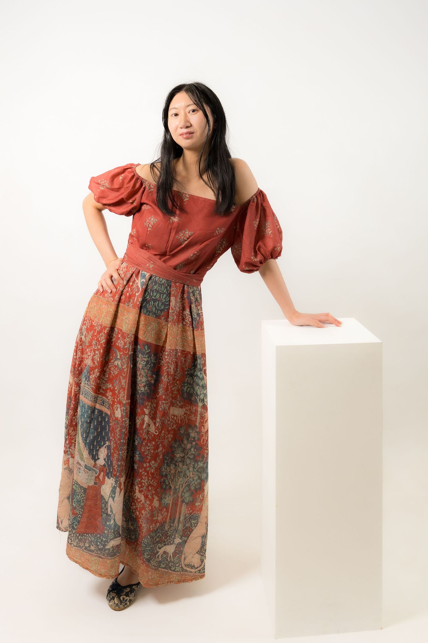 Young Asian woman in red off-shoulder top and floral maxi skirt posing confidently in a studio setting.