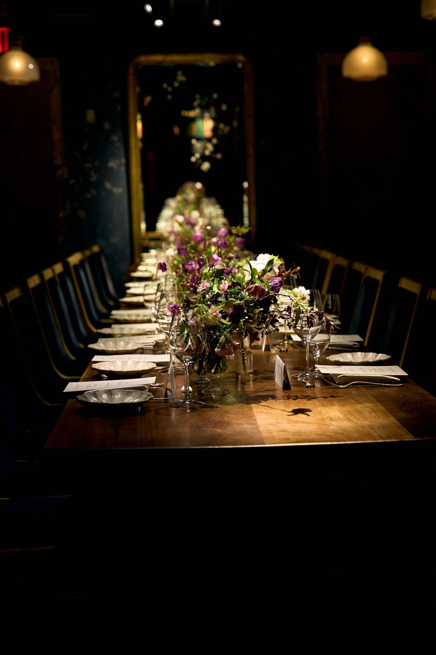 Elegant long dining table set for a formal dinner with purple floral centerpieces in a dimly lit restaurant.