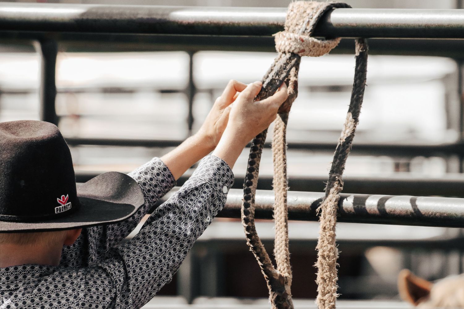 Cowboy in hat handling braided rope at a rodeo arena fence.