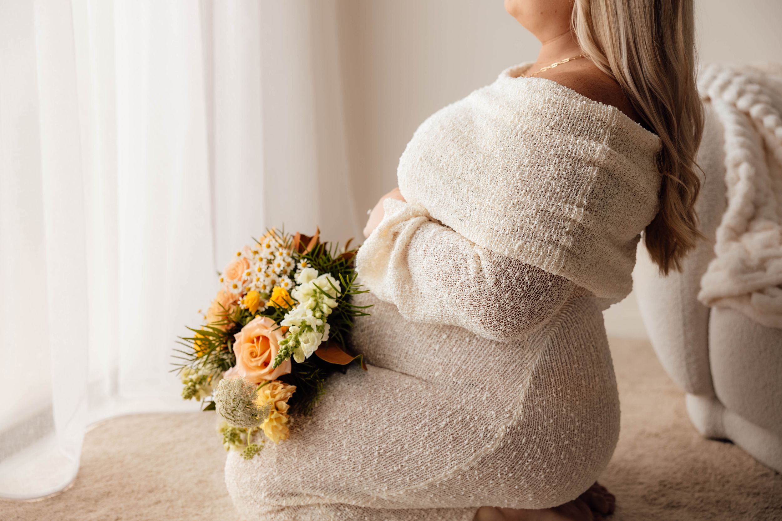 Pregnant woman in white knit dress holding colorful flower bouquet against her baby bump.