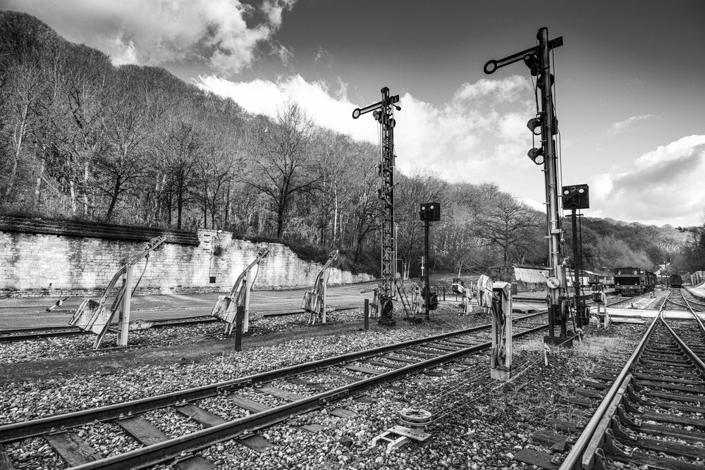 Black and white HDR photo of vintage railway signal posts along old train tracks with wooded hills behind.