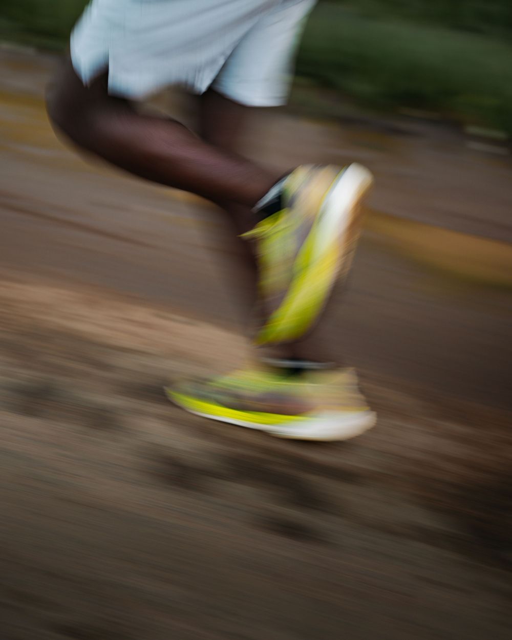 A motion-blurred close-up of a runner wearing yellow sneakers and white shorts on a path.