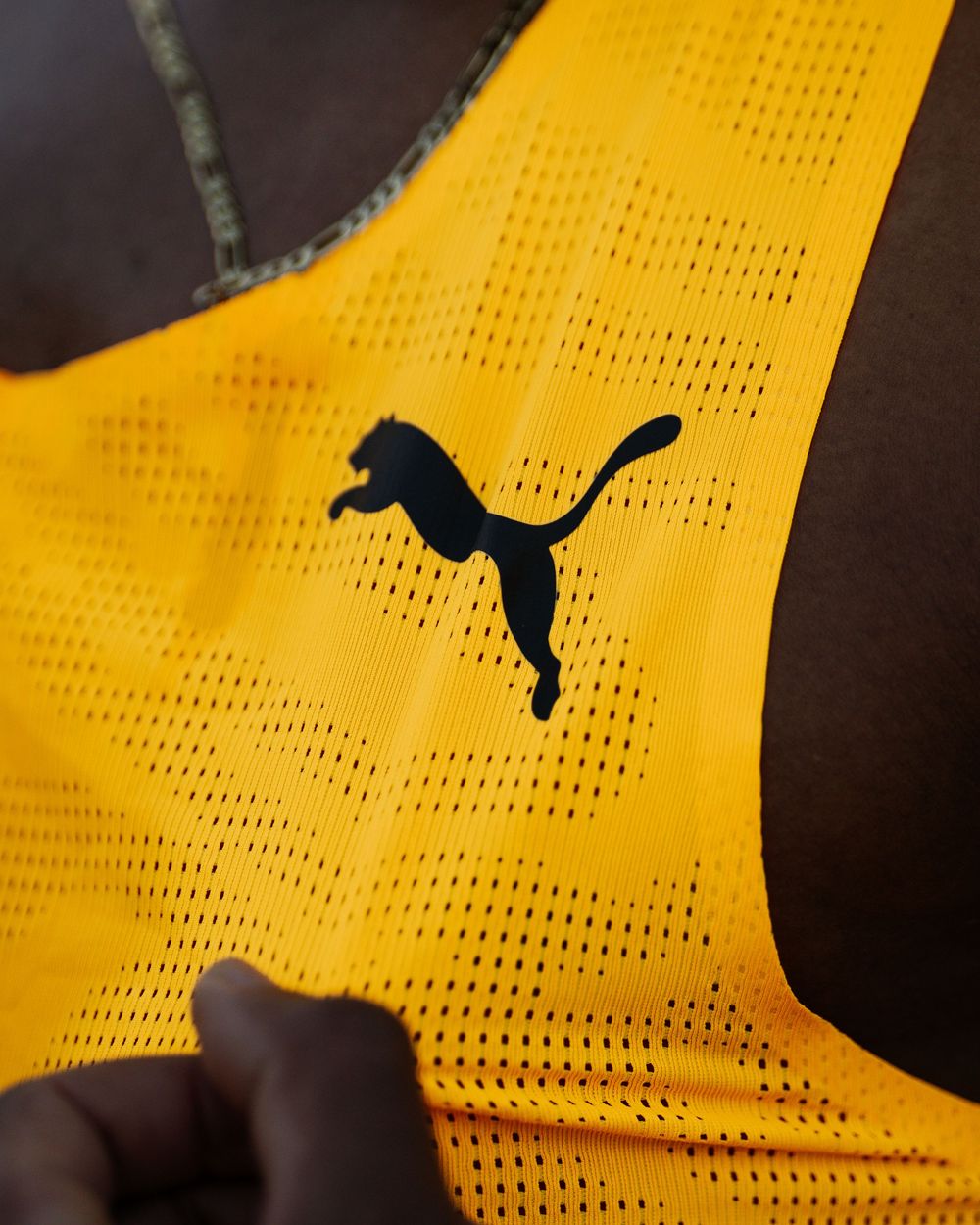 A close-up of a yellow perforated Puma athletic vest featuring the iconic Puma cat logo.
