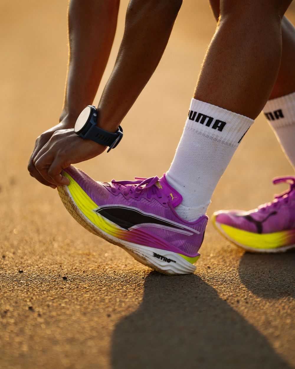 A close-up of hands adjusting purple Puma running shoes with neon soles on a track.