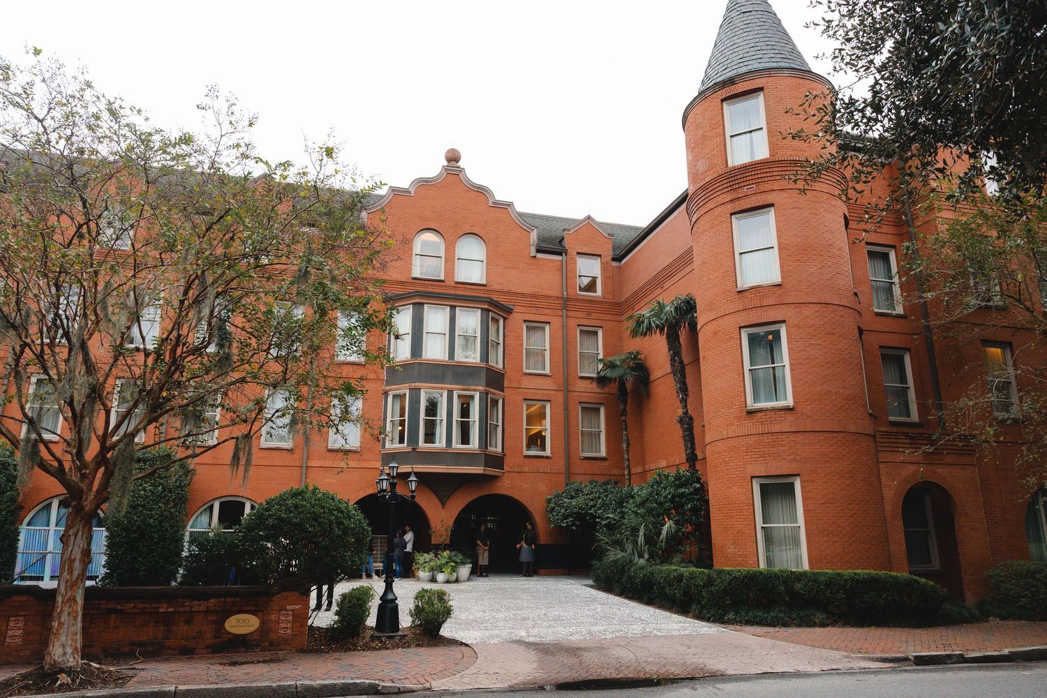 Historic red brick hotel with Victorian architecture, turret, and lush greenery on a quiet street.