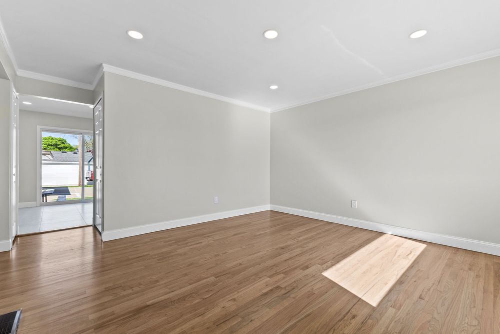 Spacious empty room with hardwood floors, recessed lighting, crown molding, and view to patio door.