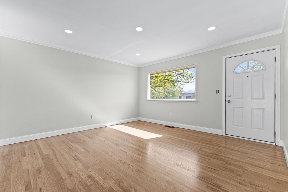 Bright empty room with light hardwood floors, recessed lighting, crown molding, and front entry door.