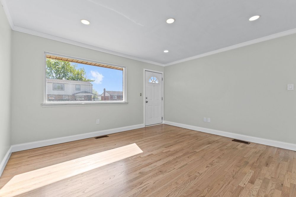 Sun-filled empty room with light hardwood floors, recessed lighting, crown molding, and dual windows.