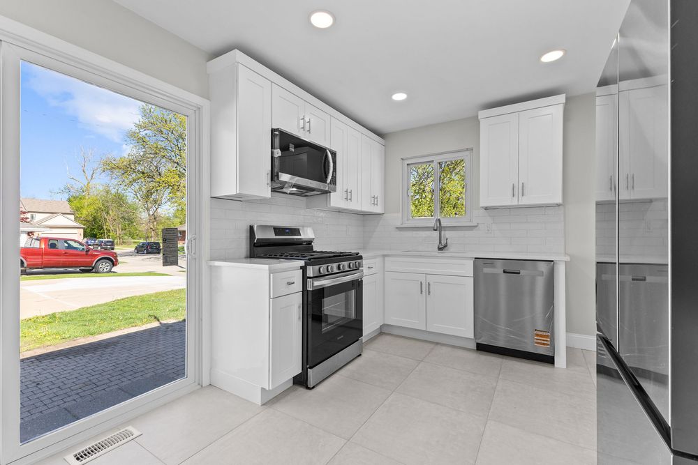 Modern kitchen with white cabinets, stainless steel appliances, tile floors, and large sliding door.