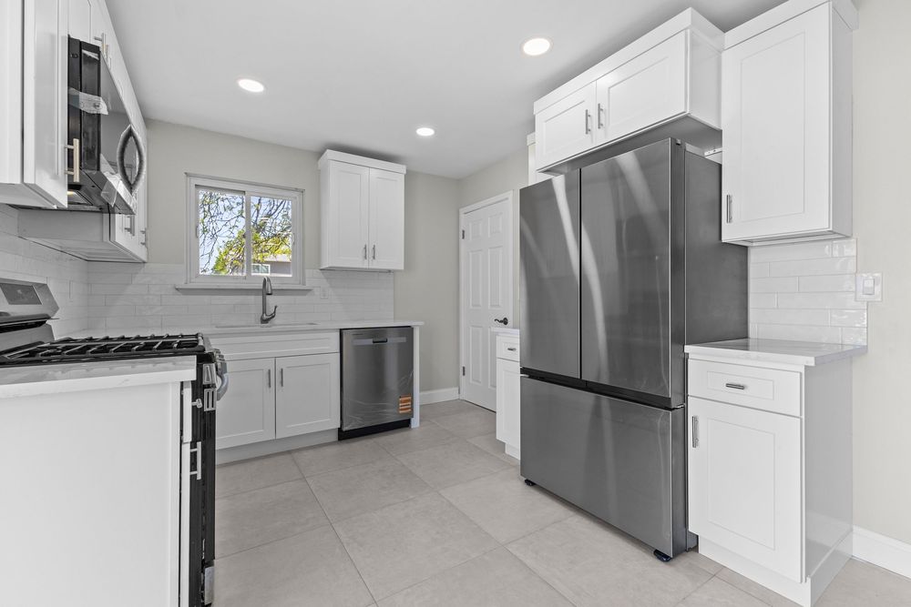 Bright kitchen featuring white cabinets, stainless steel refrigerator, tile floors, and subway backsplash.