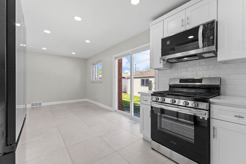 Modern kitchen with stainless steel appliances, white cabinets, subway tile backsplash, and sliding glass door to backyard.