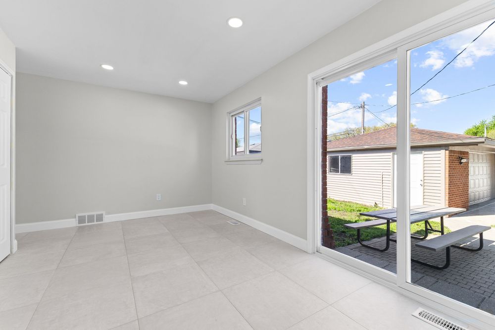 Bright empty room with large sliding glass door leading to a sunny backyard patio with picnic table.