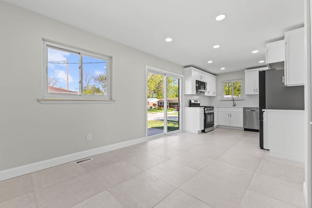 Open living area with white kitchen, stainless appliances, sliding glass door, and large light-filled windows.