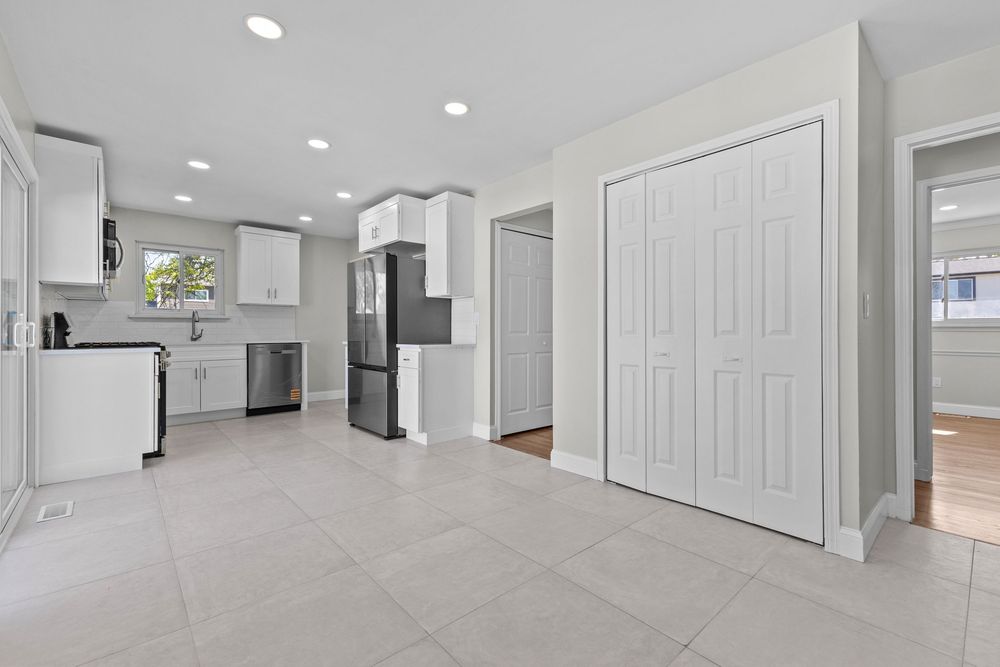 Spacious kitchen area with white cabinets, stainless steel refrigerator, and large white closet doors.