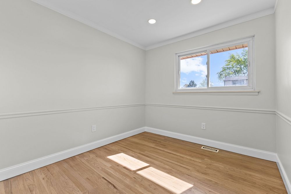 Empty bedroom with light hardwood floors, crown molding, recessed lighting, and bright window.