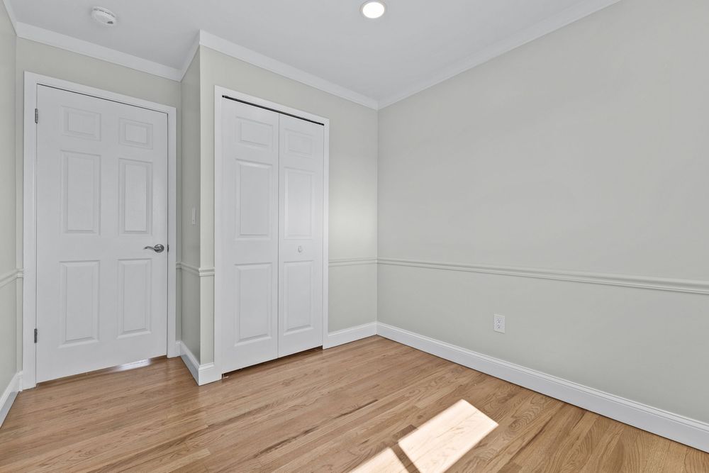 Vacant bedroom featuring hardwood floors, crown molding, closet with white double doors, and recessed lighting.