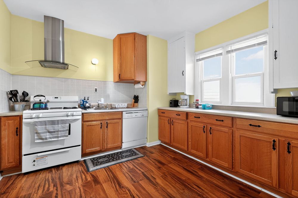 Kitchen with wood cabinets, white appliances, wall-mounted range hood, and hardwood floors.