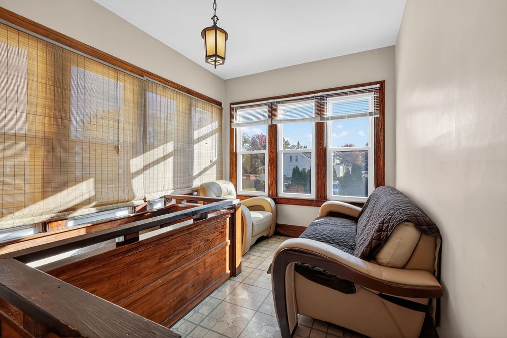 Sun-filled enclosed porch with tile floors, wooden desk, leather chair, and large windows with neighborhood views.