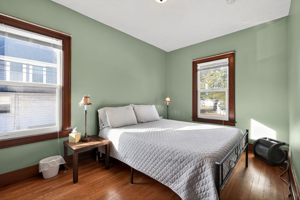 Bedroom with sage green walls, hardwood floors, black metal bed frame, and two windows.