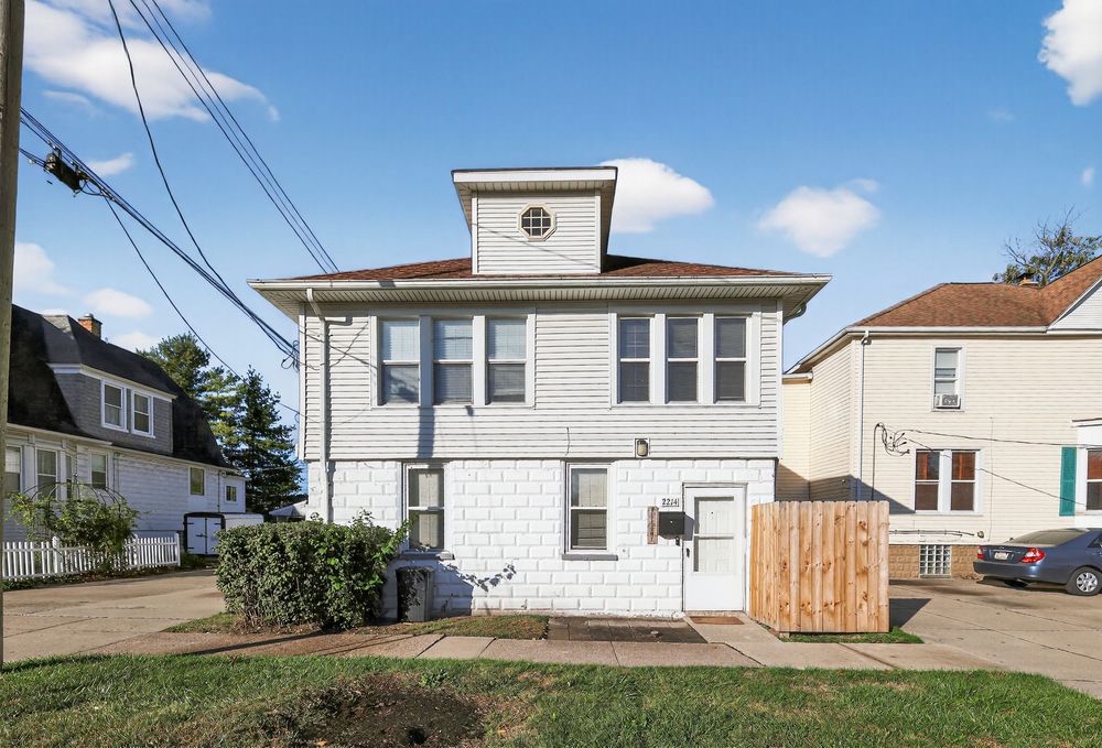 Two-story white brick home with dormer window, small front yard, and wood privacy fence.