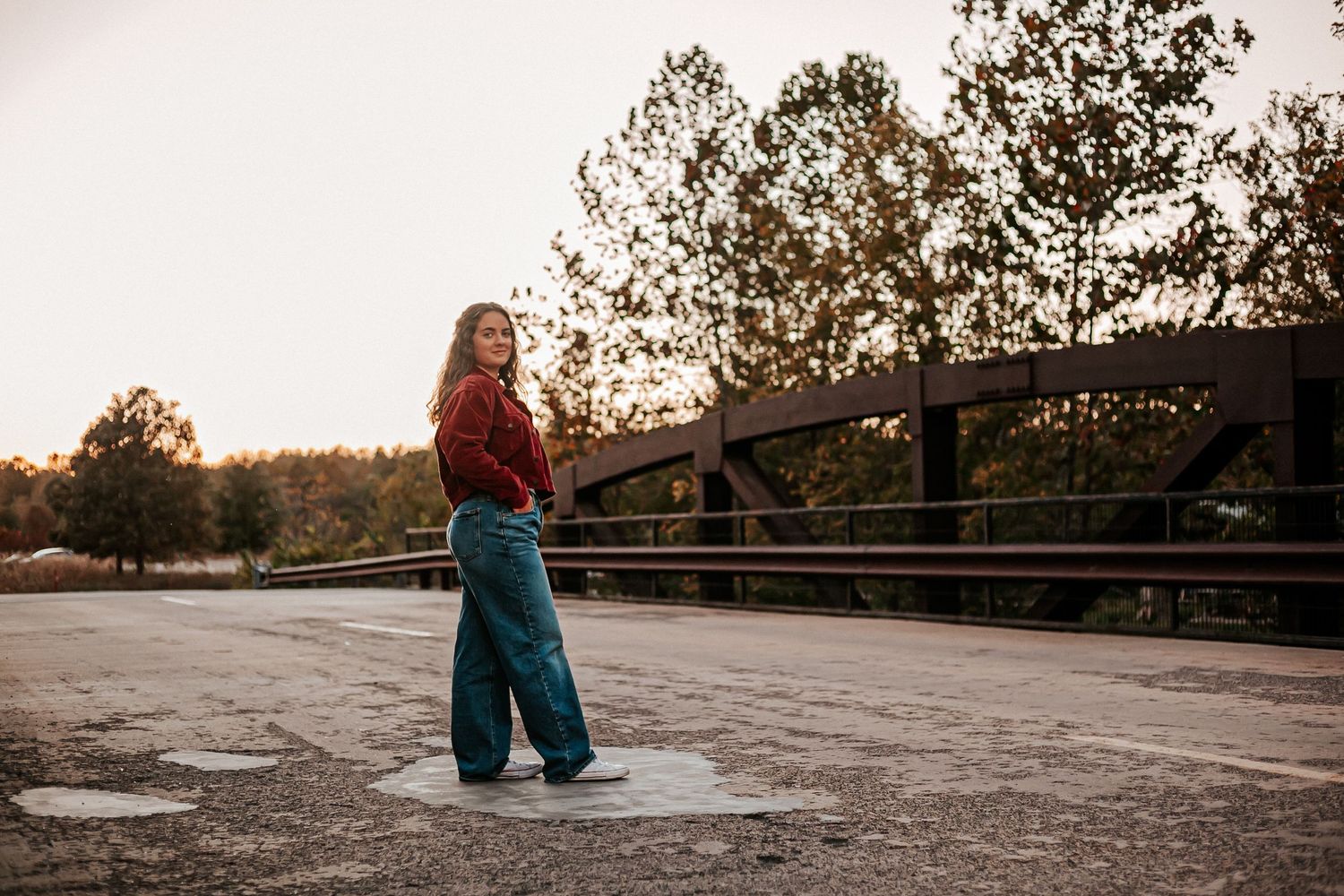 Young woman in teal wide-leg pants and red top standing on a bridge at golden hour.