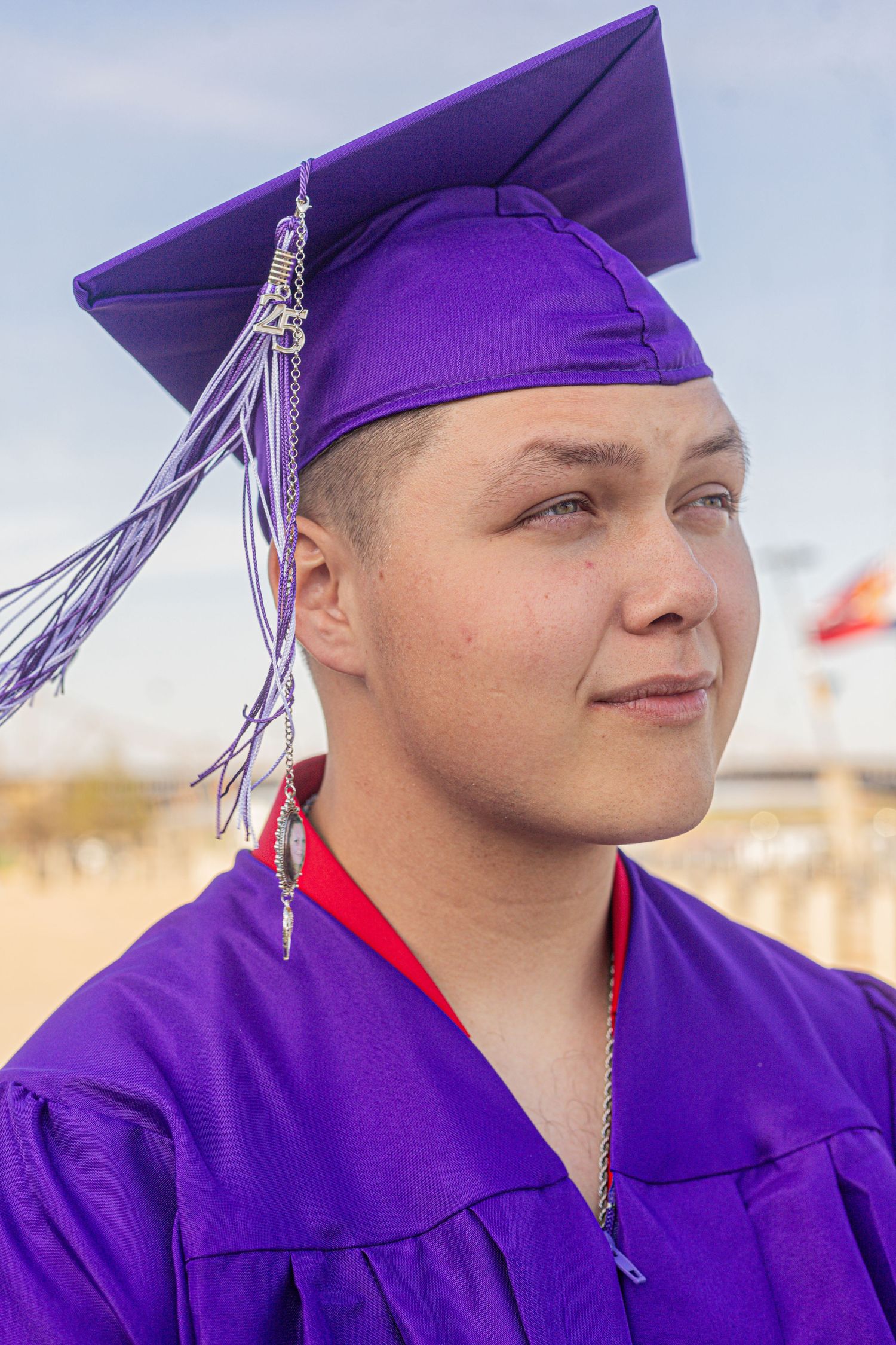 Young graduate in purple cap and gown smiling confidently outdoors during graduation ceremony.