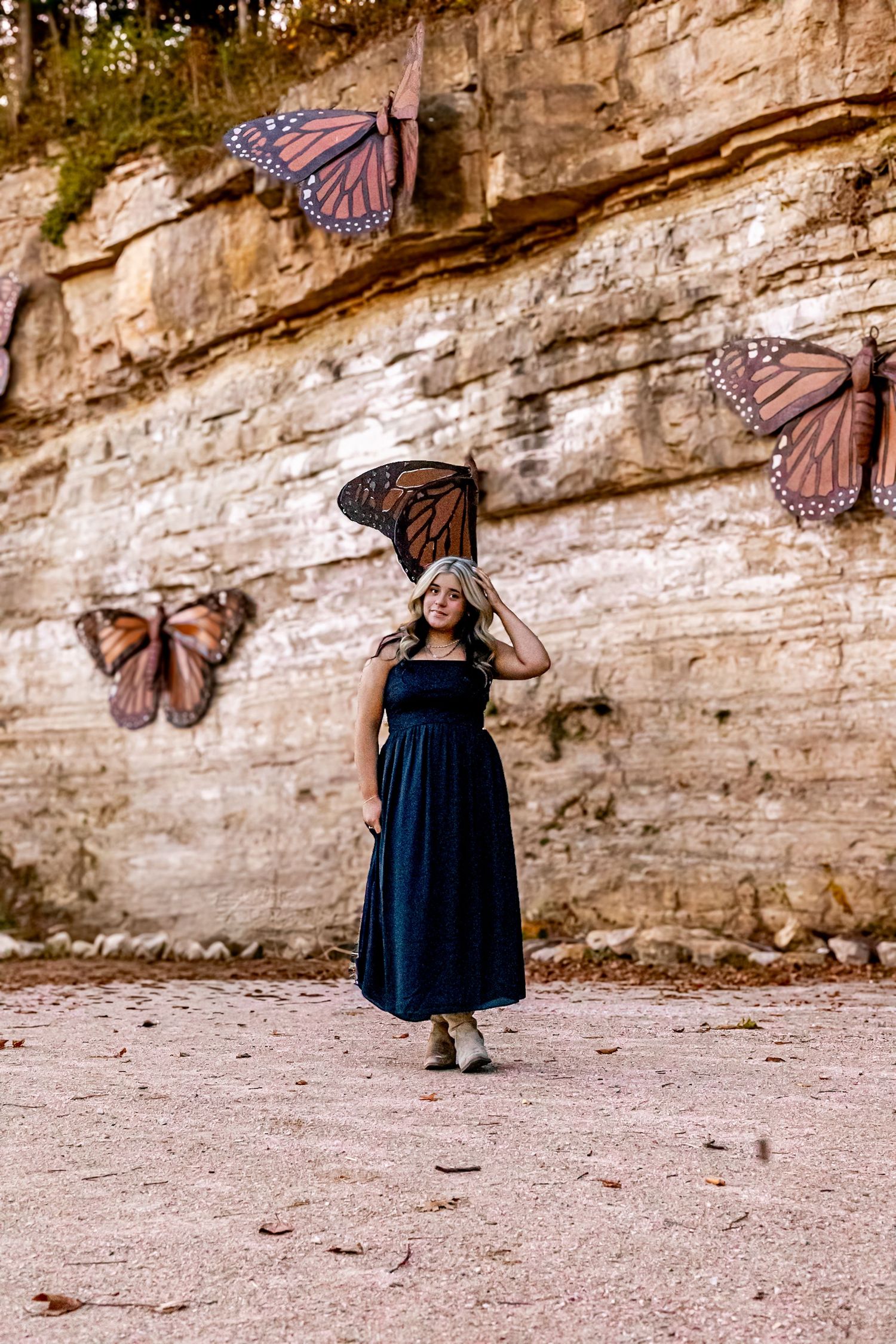 Woman in navy dress poses before a rock wall adorned with large monarch butterfly murals.