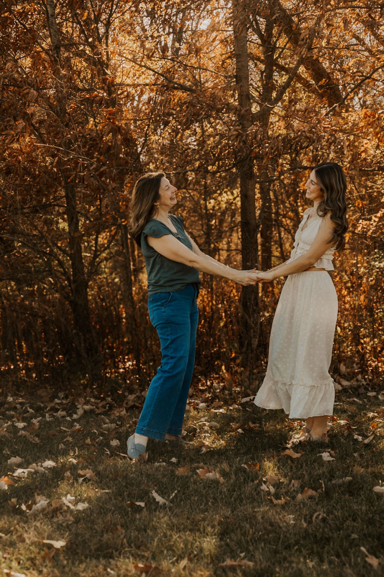 Two women holding hands and dancing together in autumn forest with golden foliage.