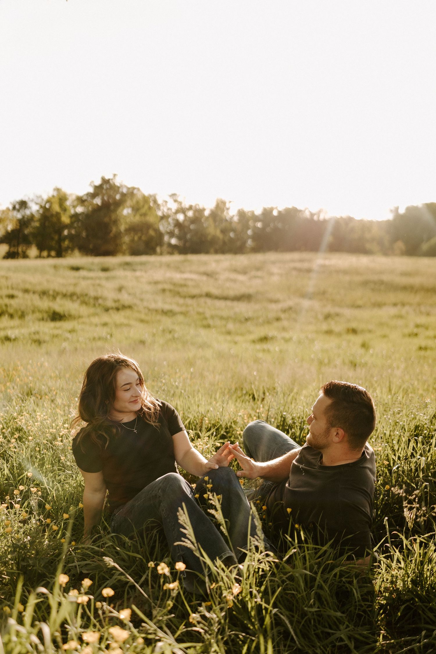 Couple sits together in golden sunlit meadow holding hands at sunset.