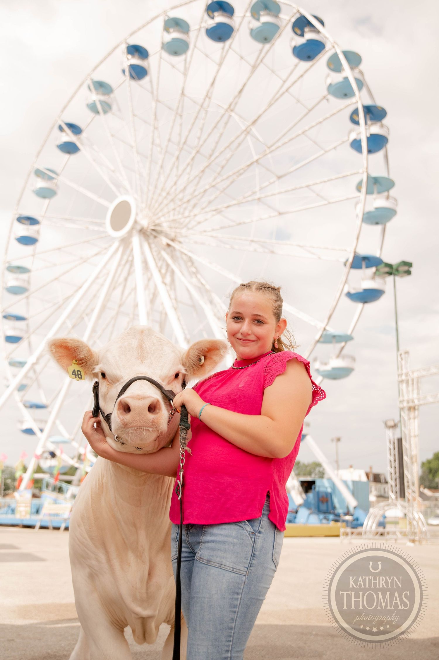 Girl in pink top leads white calf at county fair with large Ferris wheel backdrop, likely a 4-H livestock show.