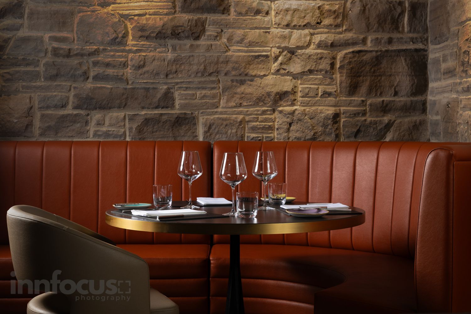 Elegant restaurant booth with terracotta leather seating, wine glasses, and rustic stone wall backdrop.
