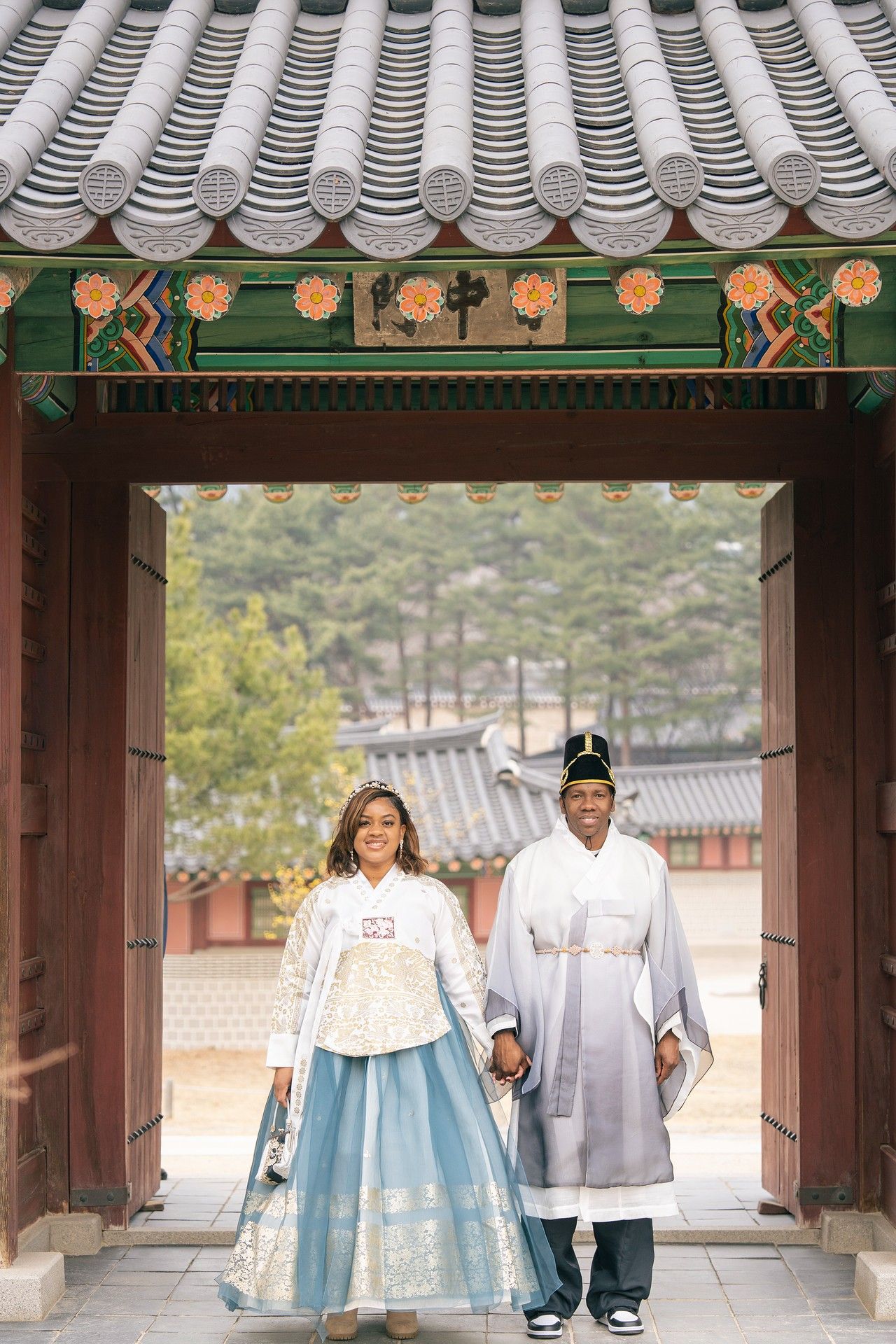 Couple wearing traditional Korean hanbok attire walking through ornate palace gate at historic Korean temple.