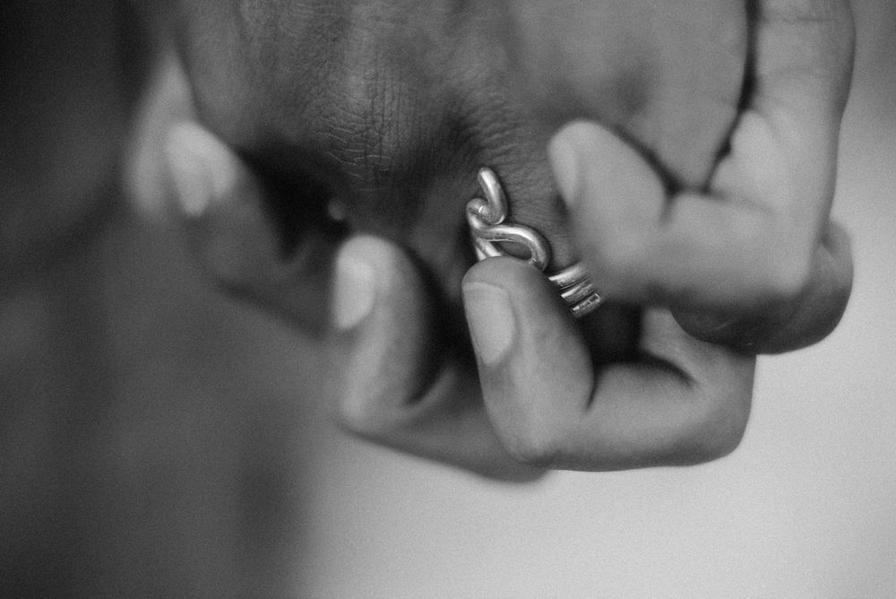 Close-up black and white photo of hands holding small silver rings between fingers.