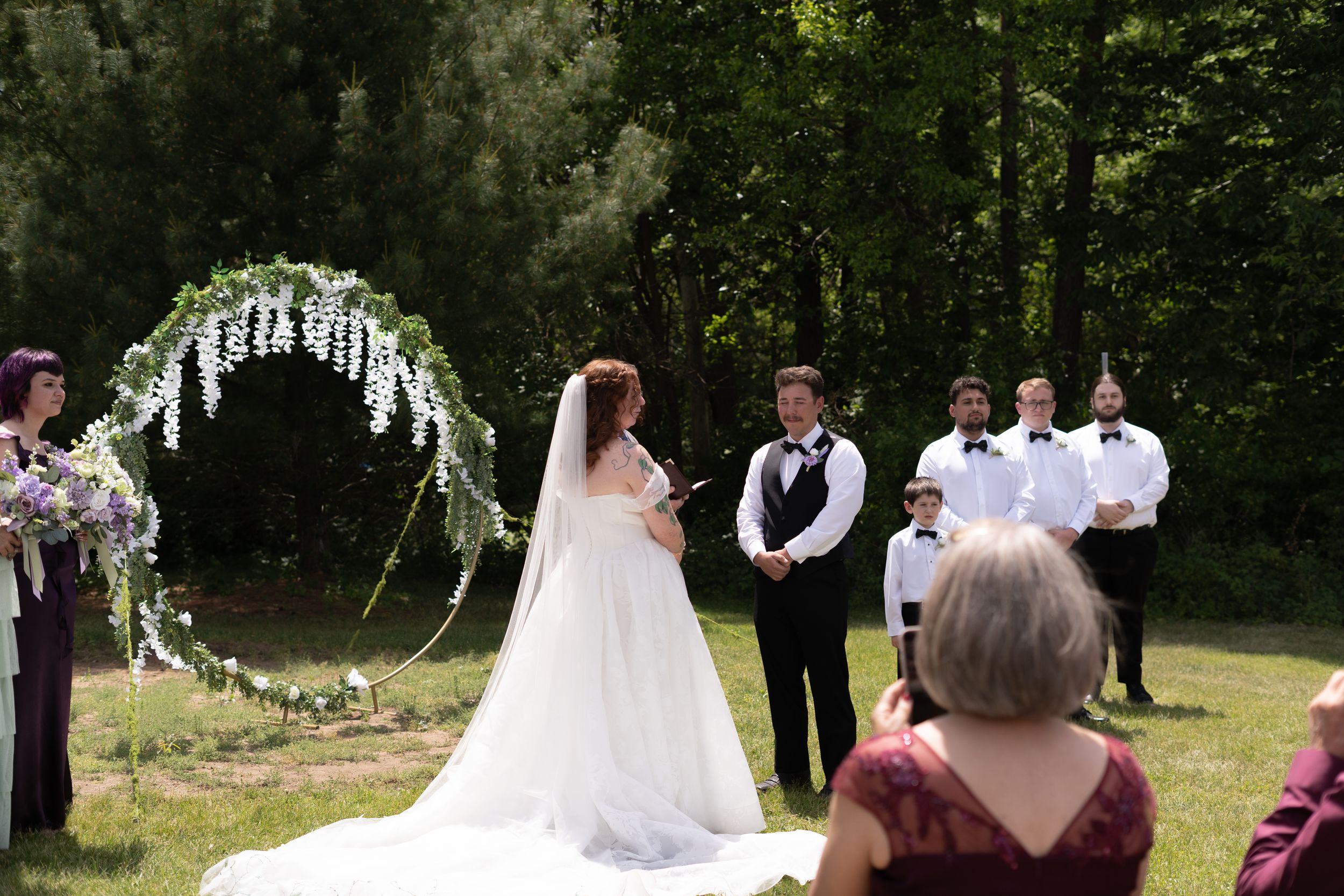 Bride and groom exchange vows under floral arch at outdoor garden wedding ceremony.