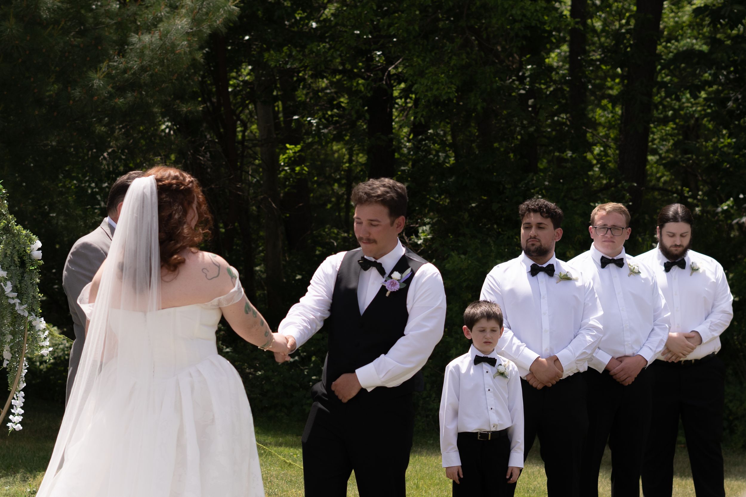 Bride and groom hold hands at altar with groomsmen in black bow ties standing nearby.