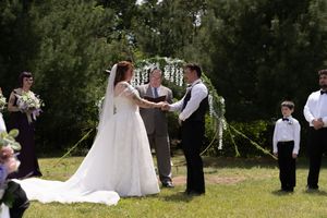 Bride and groom exchange vows under floral arch during outdoor garden wedding ceremony.