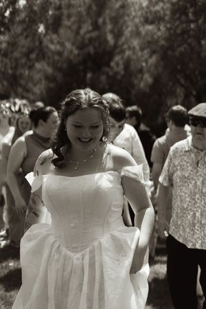 Black and white photo of a smiling bride in a white gown walking with guests at her wedding.