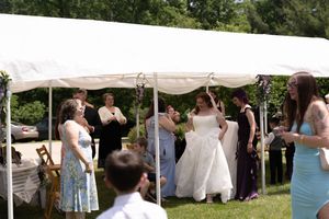Bride in white wedding gown celebrates with guests under white tent at outdoor wedding reception.