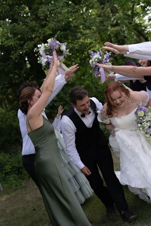 Joyful wedding party celebrating with bouquets raised as bride and groom walk together outdoors.
